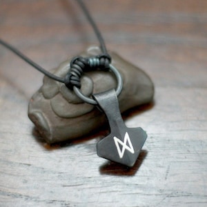 May include: A black leather cord necklace with a silver metal ring and a black metal pendant shaped like a hammer with a white rune symbol.