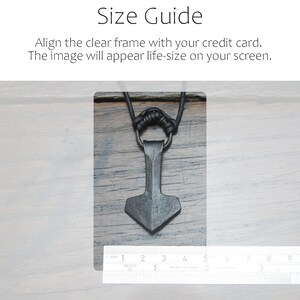 May include: A dark gray, hand-forged metal pendant shaped like a hammer, suspended from a black cord. A metal ruler is positioned at the bottom, showing the pendant is approximately 1.5 inches wide and 2.5 inches tall. Text reads: Size Guide. Align the clear frame with your credit card. The image will appear life-size on your screen.