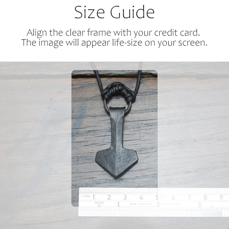 May include: A dark gray, hand-forged metal pendant shaped like a hammer, suspended from a black cord. A metal ruler is positioned at the bottom, showing the pendant is approximately 1.5 inches wide and 2.5 inches tall. Text reads: Size Guide. Align the clear frame with your credit card. The image will appear life-size on your screen.