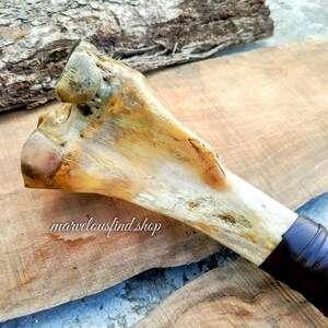 May include: A bone-handled tool with a natural, off-white color and dark brown leather wrapping. The bone has a textured surface and is set against a wooden background. The text "marvelousfind shop" is visible.