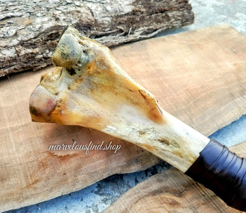 May include: A bone-handled tool with a natural, off-white color and dark brown leather wrapping. The bone has a textured surface and is set against a wooden background. The text "marvelousfind shop" is visible.