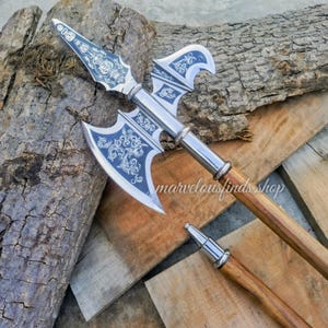 May include: A medieval-style polearm with a silver blade and a wooden handle. The blade features intricate, decorative patterns in a dark blue color. The handle is made of wood. The text "marvelousfinds shop" is visible.