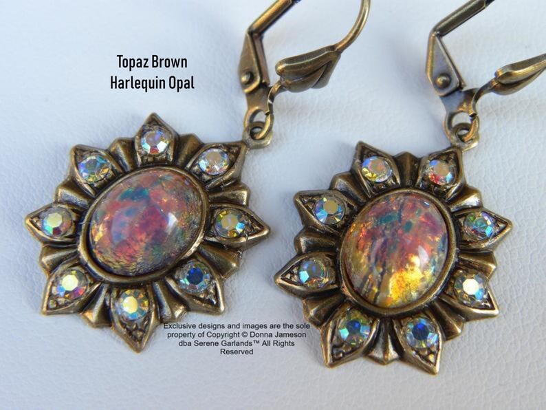 Pode incluir: Um par de brincos dourados com um caboch&atilde;o de opala harlequim marrom top&aacute;zio engastado em um design de raios de sol com detalhes em cristal transparente.  "Topaz Brown Harlequin Opal" e "Exclusive designs and images are the sole property of Copyright &copy; Donna Jameson dba Serene Garlands&trade; All Rights Reserved" est&atilde;o impressos na imagem.
