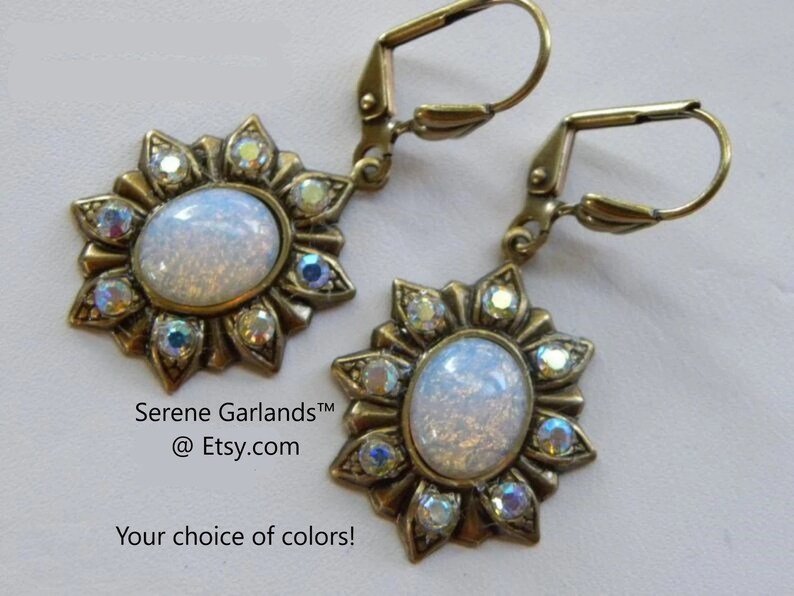 Pode incluir: Um par de brincos dourados com uma pedra de opala branca cercada por strass transparentes em um design de raios de sol. Os brincos t&ecirc;m um fecho de alavanca. Serene GarlandsTM @Etsy.com Sua escolha de cores!