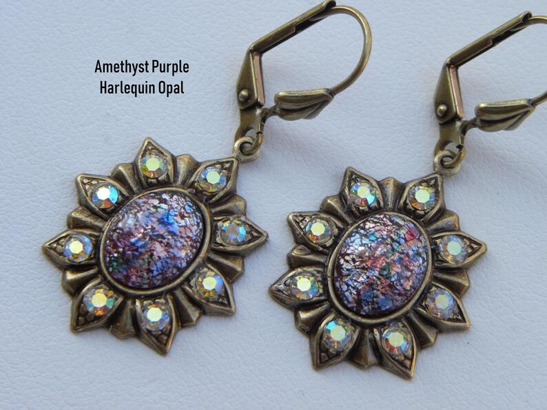 Pode incluir: Um par de brincos de bronze com uma pedra de opala p&uacute;rpura e iridescente engastada em um design de sol com strass transparentes.