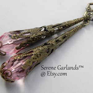 May include: A pair of dangle earrings with pink crystal teardrop beads and antique brass filigree accents. The earrings have a delicate, vintage style.