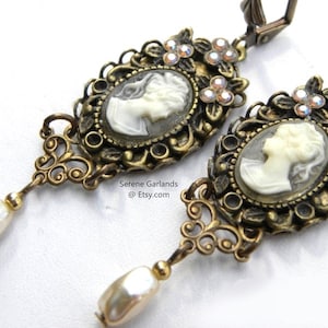 May include: Gold tone earrings with a cameo portrait, pearl accents, and crystal embellishments.  The earrings feature a delicate filigree design.