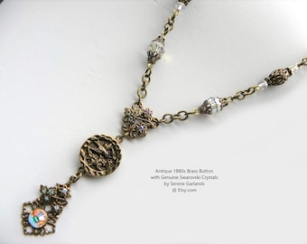 May include: A necklace featuring an antique 1880s brass button, genuine Swarovski crystals, and a brass chain. The text reads: Antique 1880s Brass Button with Genuine Swarovski Crystals by Serene Garlands @ Etsy.com. The design includes metal filigree.