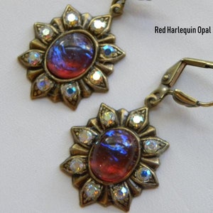 Pode incluir: Um par de brincos em tom dourado com uma gema de opala vermelha harlequim engastada em um design de raios de sol com strass transparentes.