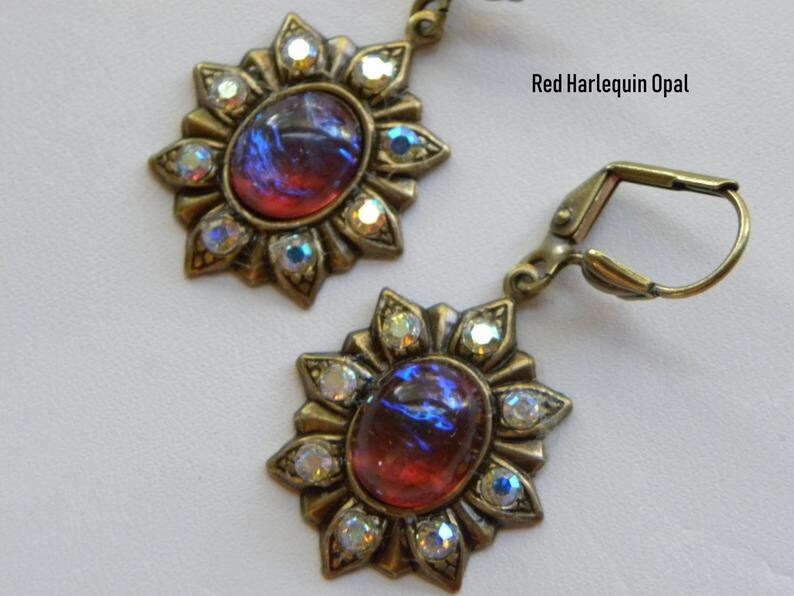 Pode incluir: Um par de brincos em tom dourado com uma gema de opala vermelha harlequim engastada em um design de raios de sol com strass transparentes.