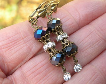 May include: A pair of dangle earrings with black and iridescent glass beads, gold-tone metal accents, and clear crystal accents.
