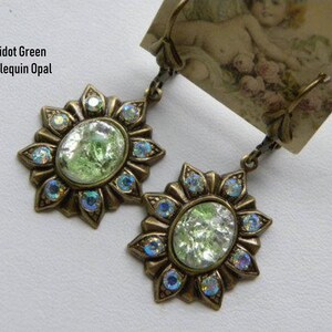 Pode incluir: Um par de brincos com uma pedra de opala verde engastada em um design de bronze em forma de sol com acentos azuis iridescentes. Os brincos s&atilde;o etiquetados como "Peridot Green Harlequin Opal".