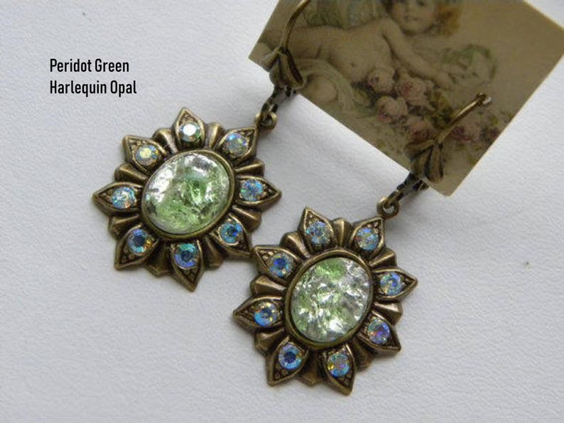 Pode incluir: Um par de brincos com uma pedra de opala verde engastada em um design de bronze em forma de sol com acentos azuis iridescentes. Os brincos s&atilde;o etiquetados como "Peridot Green Harlequin Opal".