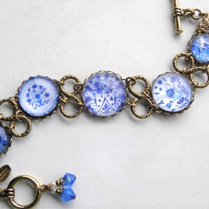 May include: A bracelet featuring five circular blue and white floral patterned glass cabochons set in antique brass metal frames. The links are connected by ornate brass rings, and the piece includes a toggle clasp with two small blue crystal beads.