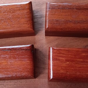 May include: Four rectangular wooden boxes with a polished reddish-brown finish and visible wood grain. Each box features a smooth, beveled lid and a consistent, uniform shape, arranged in a two-by-two grid pattern on a flat surface.
