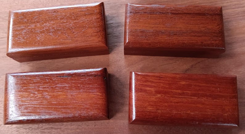 May include: Four rectangular wooden boxes with a polished reddish-brown finish and visible wood grain. Each box features a smooth, beveled lid and a consistent, uniform shape, arranged in a two-by-two grid pattern on a flat surface.