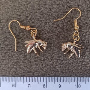 May include: A pair of gold-toned bee-shaped dangle earrings with hook-style wires. The bee charms feature detailed wings and body segments. A ruler is visible at the bottom, showing the bee charms measure approximately 0.75 inches in width.