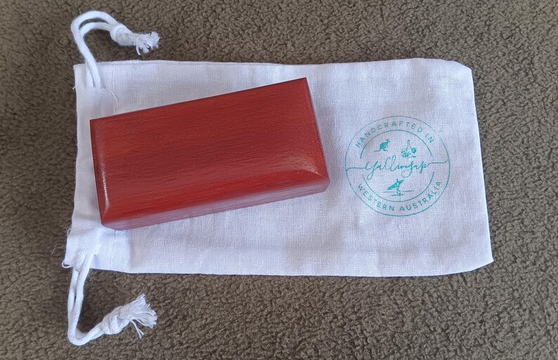 May include: A rectangular reddish-brown wooden box with a smooth finish resting on a white fabric drawstring pouch. The pouch features a circular teal logo with the text Handcrafted in Western Australia and Yallingup with small icons.