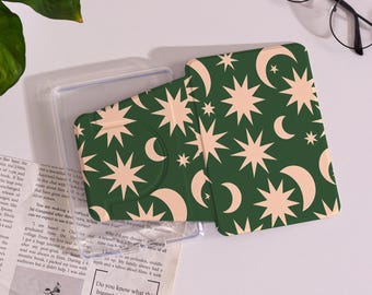 May include: A green phone case with a celestial pattern of cream-colored stars and crescent moons. The case is open, revealing the interior. The design is repeated on the case's exterior. A clear plastic case is also visible.
