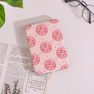 May include: A pink notebook with a pattern of disco balls in shades of pink and red, and small white stars. The notebook is rectangular and has rounded corners. The background is a light pink color.