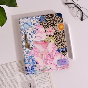 May include: A decorative journal with a colorful design featuring a pink cocktail, leopard print, and floral patterns. The journal has a blue and white floral pattern, a leopard print section, and the number 888.