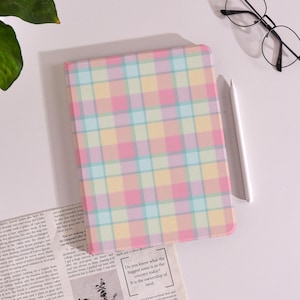 May include: A pastel-colored tablet case with a plaid pattern in pink, yellow, blue, and green. The case is rectangular and has rounded corners. A white stylus and black-framed glasses are next to the case. The text on the newspaper says "Do you know what the biggest issue is in the country today? It is the ownership of land."