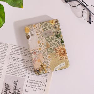 May include: A decorative journal with a floral and sun design. The cover features a collage of botanical illustrations, a sun face, and the text "we were infinite". The journal is on a white surface.