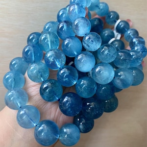 Puede incluir: Una colección de cuentas de piedras preciosas de aguamarina azul claro. Las cuentas redondas tienen una calidad translúcida, con variaciones de color y patrones internos. Las cuentas están ensartadas, formando una pulsera o collar.
