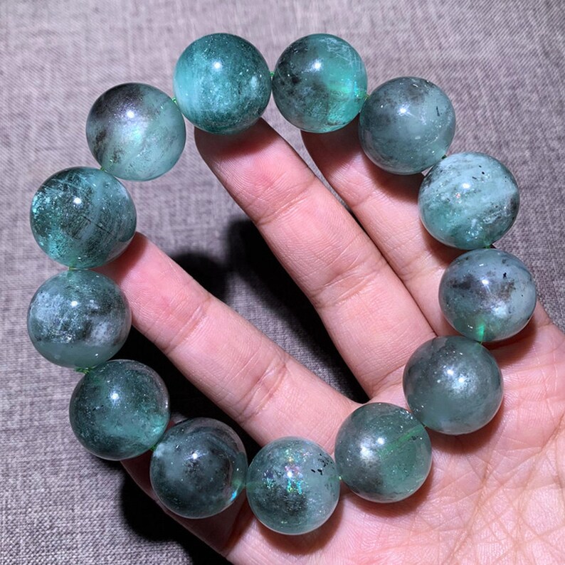 Peut inclure: Un bracelet compos&eacute; de perles rondes et polies dans des tons de vert translucide et de gris fonc&eacute;. Les perles pr&eacute;sentent des inclusions internes et des niveaux de clart&eacute; variables, cr&eacute;ant un aspect marbr&eacute; dans tout l'arrangement circulaire.