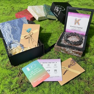 Peut inclure: Une bo&icirc;te cadeau noire contenant un bracelet de perles bleues, une carte beige avec une fleur s&eacute;ch&eacute;e et une carte d&eacute;grad&eacute;e avec le texte I GIVE MYSELF PERMISSION TO REST AND RECHARGE. Une seconde bo&icirc;te noire contient un bracelet gris fonc&eacute;.