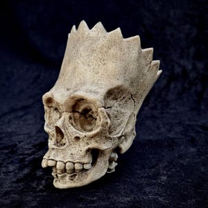 Może przedstawiać: Biała ceramiczna czaszka z kolczastą koroną na górze. Czaszka ma szczegółową twarz z zębami i oczodołami.