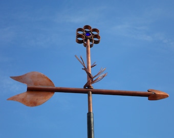 May include: A copper weather vane with a stylized flower design featuring a blue glass center. The flower is atop a copper stem with a twisted copper wire design. The vane has a copper arrow pointing to the right.