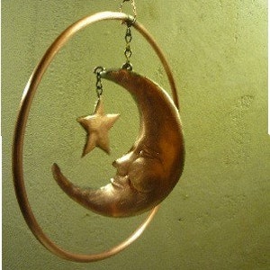 May include: A copper moon and star mobile with a sleeping face on the moon. The mobile is hanging from a copper chain.