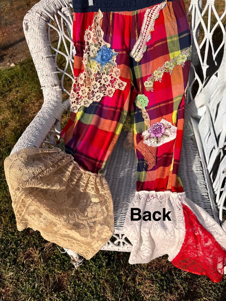 May include: Colorful plaid pants with lace and floral appliqu&eacute;s. The pants feature a mix of red, pink, yellow, and blue plaid fabric, with decorative lace patches and floral accents. The bottom of the pants have a flared, lace trim. The word "Back" is visible.