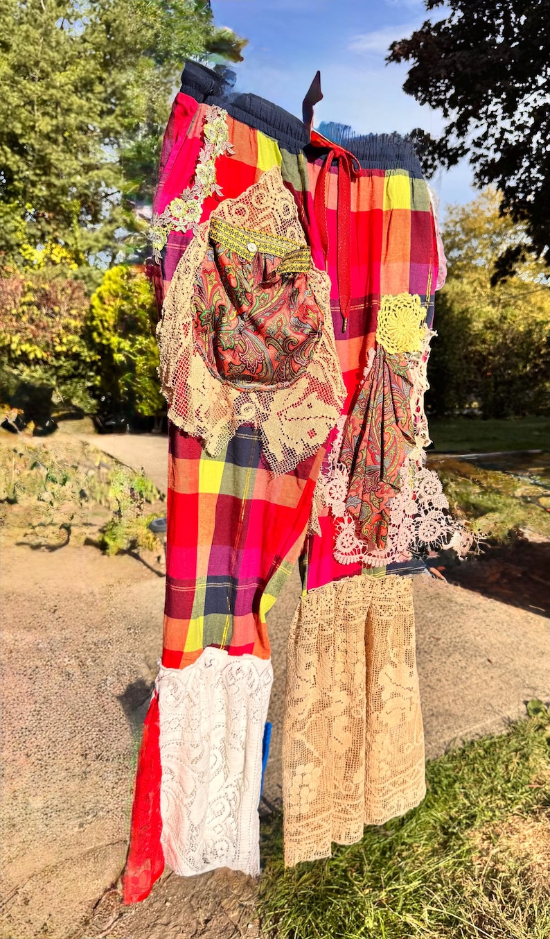 May include: Colorful patchwork pants with a plaid pattern in red, yellow, and purple. The pants feature lace and paisley fabric accents, with a drawstring waist. A unique, handmade garment.