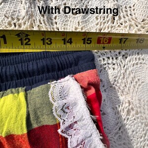 May include: Close-up of colorful shorts with a drawstring. The shorts have a navy blue waistband and are measured at 15 inches relaxed waist, with a width of 12-21 inches. The shorts are trimmed with white lace.