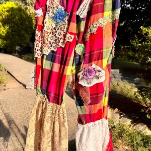 May include: Colorful plaid pants with lace and floral embellishments. The pants feature a red, yellow, and blue plaid pattern, with patches of lace and embroidered flowers. The pants have a drawstring waist and flared lace cuffs.