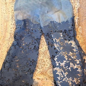 Puede incluir: Vaqueros de mezclilla azul claro con un diseño único. La parte inferior de los vaqueros presenta una superposición de encaje floral detallado en un tono azul a juego. Los vaqueros tienen un efecto de lavado descolorido.