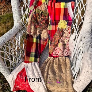 May include: Colorful patchwork pants with a red drawstring waist. The pants feature a mix of plaid, paisley, and lace fabrics in shades of red, yellow, and beige. A yellow crocheted flower is sewn onto the front. The word "Front" is visible on the pants.