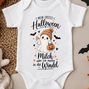 Könnte beinhalten: Ein weißer kurzärmeliger Babybody mit einer Grafik eines Geistes mit Mütze, der eine Babyflasche und einen Kürbiseimer hält. Der Text lautet: Mein erstes Halloween Milch oder ich mache in die Windel, umgeben von kleinen Fledermäusen.