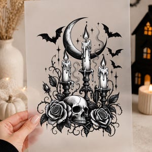May include: A black and white illustration printed on a translucent sheet featuring a human skull centred between two blooming roses. Above the skull are three lit candles in ornate holders, a crescent moon, and several flying bats with stars.