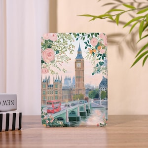 May include: A rectangular decorative item featuring a painting of London's Big Ben and the Houses of Parliament, with a red double-decker bus crossing a bridge. The artwork is framed by pink roses and greenery.