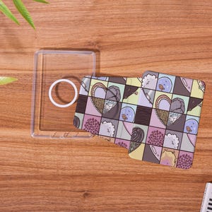May include: A clear phone case with a white circle and a patterned phone card. The card features a patchwork design with heart and bird illustrations in pastel colors, including pink, purple, and yellow.
