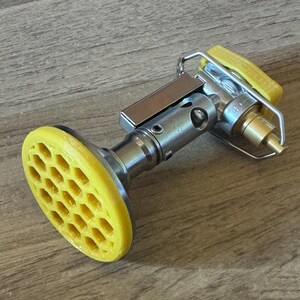 May include: A yellow and silver camping stove with a honeycomb-shaped base.