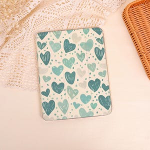 May include: A tablet case with a pattern of teal and light blue hearts on a cream background. The hearts vary in size and are scattered across the surface. The case is rectangular and has rounded corners.