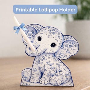 Puede incluir: Un soporte para piruletas con forma de elefante con estampado floral azul y blanco. El soporte tiene un lazo azul y sostiene una piruleta blanca. El texto "Printable Lollipop Holder" está en un rectángulo azul encima del elefante.