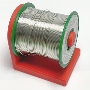May include: A spool of silver solder wire on a red and green plastic dispenser. The dispenser has a label with instructions and warnings.