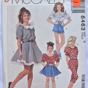 Könnte beinhalten: Ein Schnittmuster für ein Mädchenkleid mit Gingham-Muster und weißem Spitzenbesatz. Das Muster ist für Größe 8 und heißt "Easy McCall's 6463".