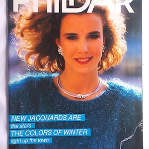 May include: Magazine cover with a woman in a teal sweater and silver jewellery. The magazine title is "PHILDAR" with the text "NEW JACQUARDS ARE the stars THE COLORS OF WINTER light up the town" in a blue box. The magazine is labeled N136.