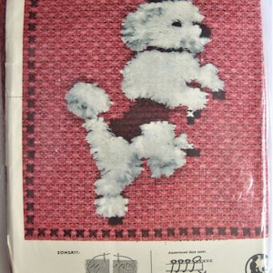 May include: A white poodle wearing a black top hat, with instructions for cross-stitch embroidery. The image is on a red background with a white border. The text on the image reads "SOMSATTI: KORSSTYGN 18.50".
